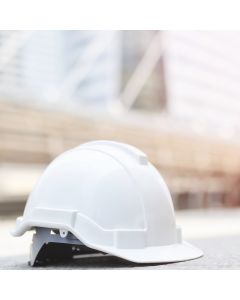 Weißer Baustellenhelm vor einem Baustellenbau auf Betonboden an der Stadt mit Sonnenlicht